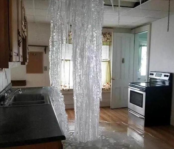 A kitchen has a large frozen waterfall coming from the ceiling with more water on the floor of the kitchen below.